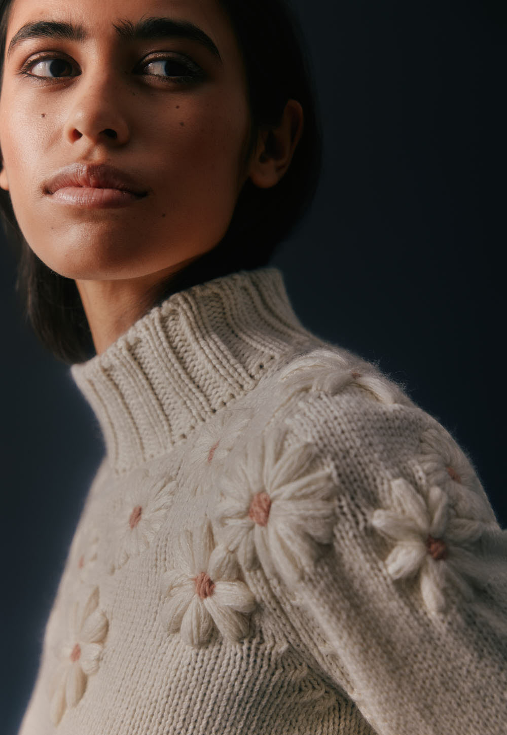 Ivory cashmere turtleneck sweater with hand-embroidered floral details, soft ribbed collar, editorial close-up
